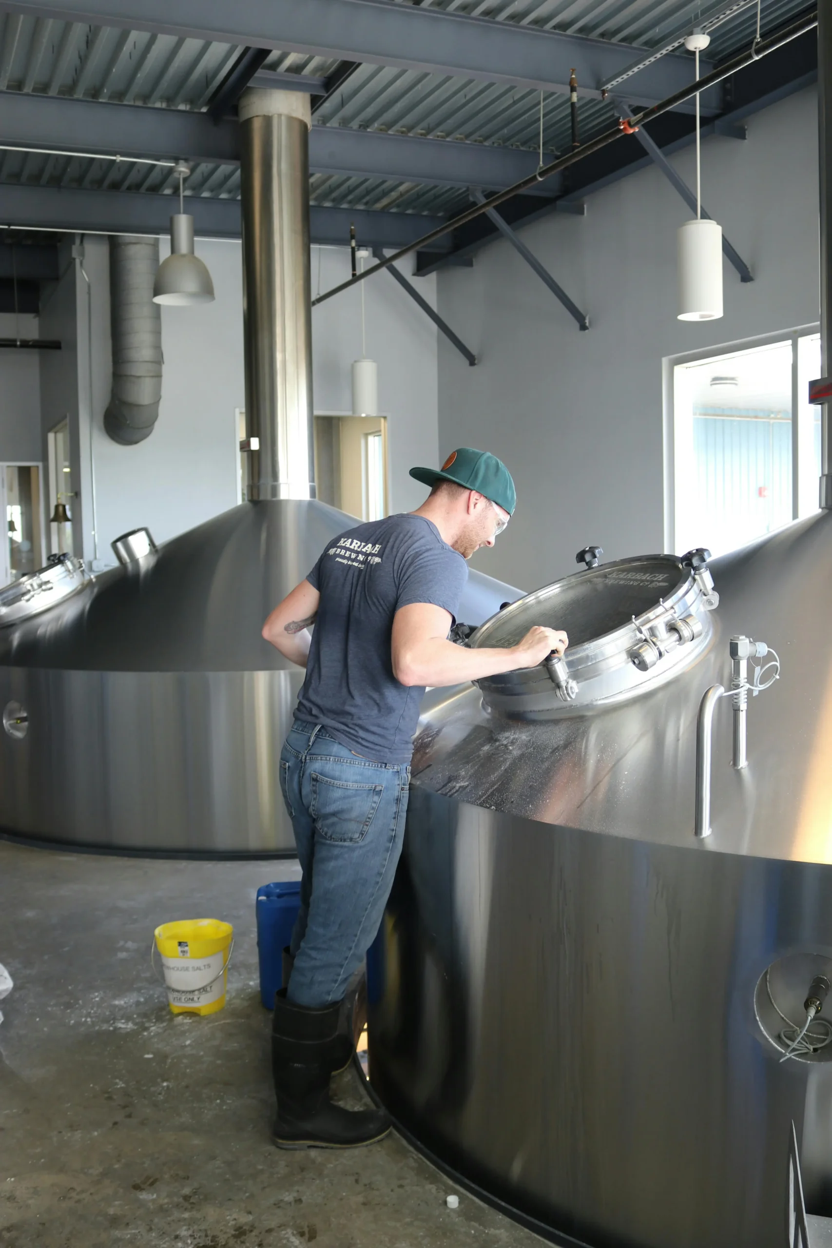 A brewery employee inspecting a brewing tank in a large brewhouse.